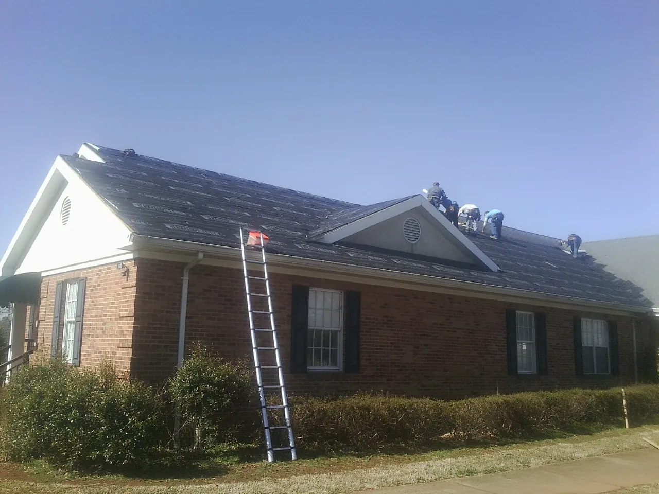 Crew tearing shingles off a brick ranch roof with a ladder set — Emergency Roof Repair work by our crew in Bagley