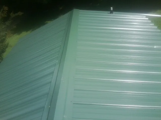 New green metal panels meeting at the ridge of a roof — Flat Roof Repair work by our crew in Bagley