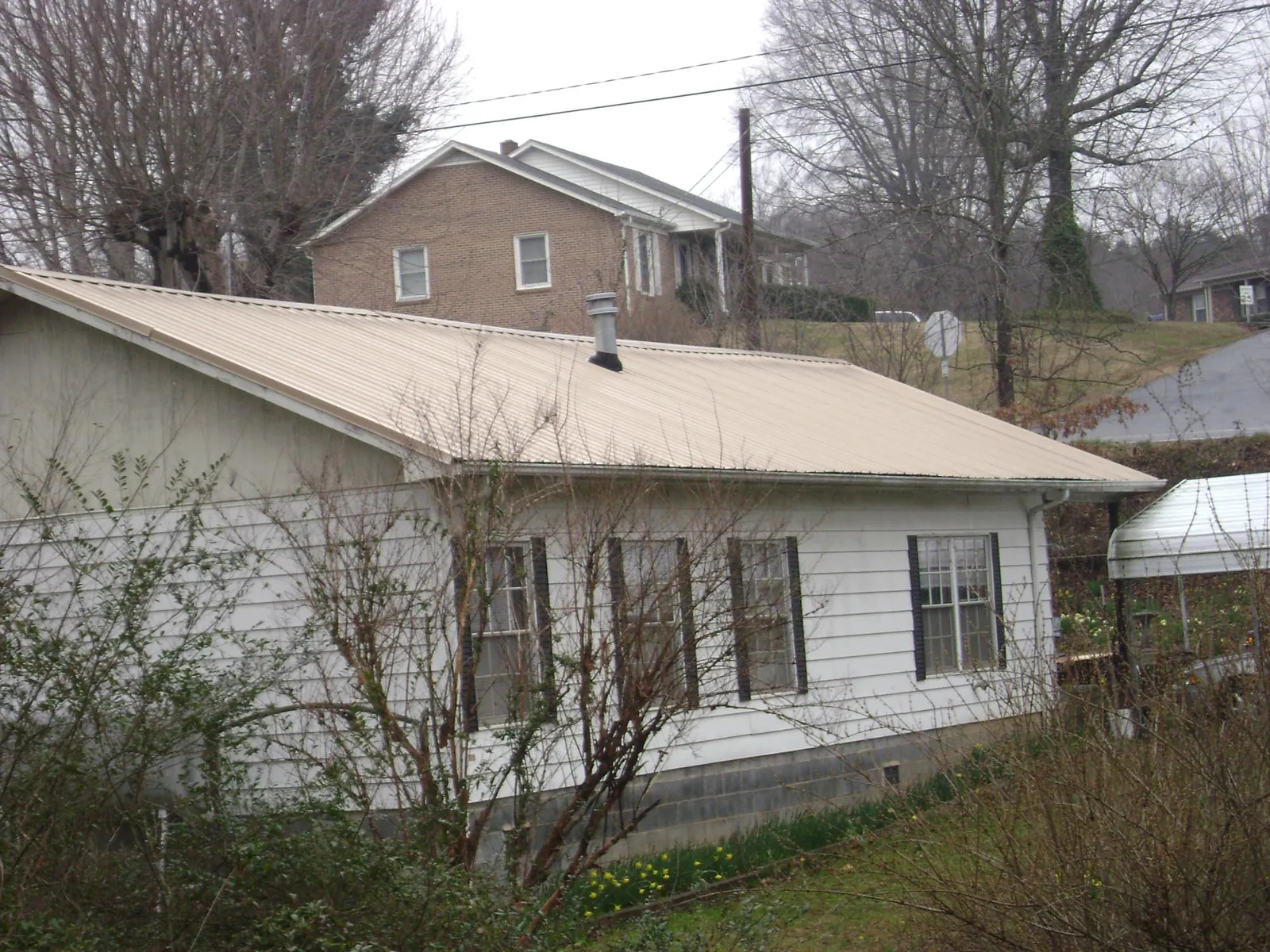 Tan metal roof on a white sided house set into a hillside — Commercial Roofing by Roofing Brothers in Bagley